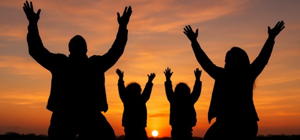 A silhouette of a Black family on their knees in a restaurant parking lot. Their hands are raised to the heavens, rejoicing.