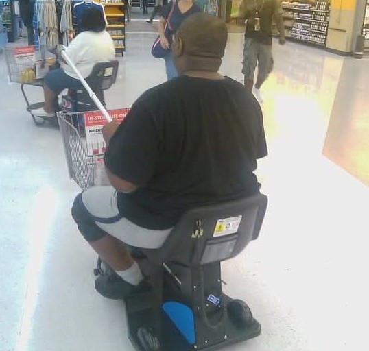Photo of a Black man in an assistance cart, jousting with his walking cane.